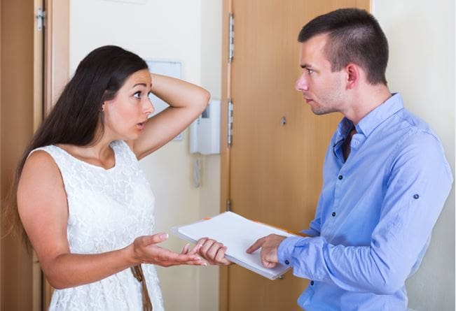 Tenant and landlord arguing over rental issues inside apartment hallway.