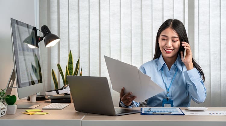 Property manager reviewing documents while on phone at office desk